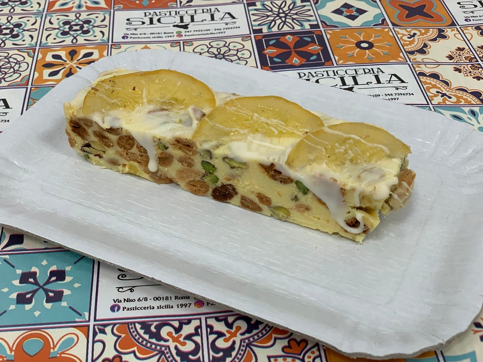 Trancio di dolce con pistacchi, mandorle e ciliegie candite su un piatto con maioliche siciliane