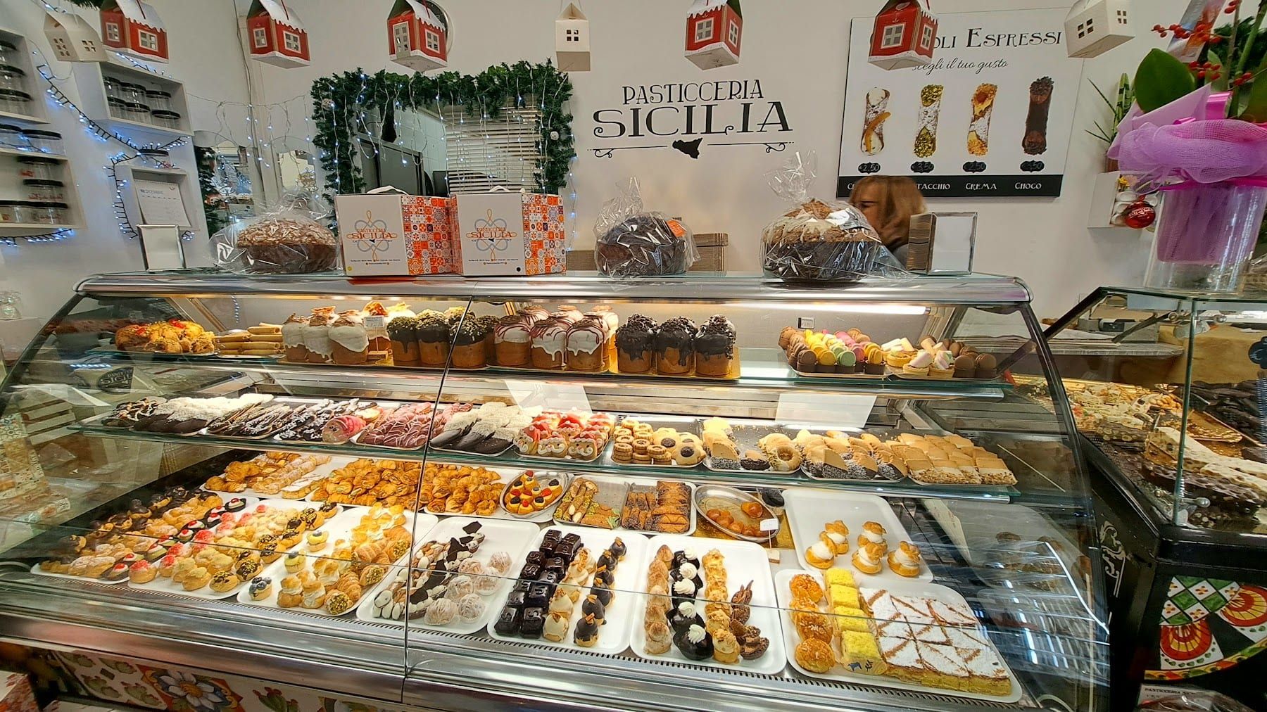 Il bancone della pasticceria con le vetrine piene di pasticcini e, sullo sfondo, l'insegna Pasticceria Sicilia